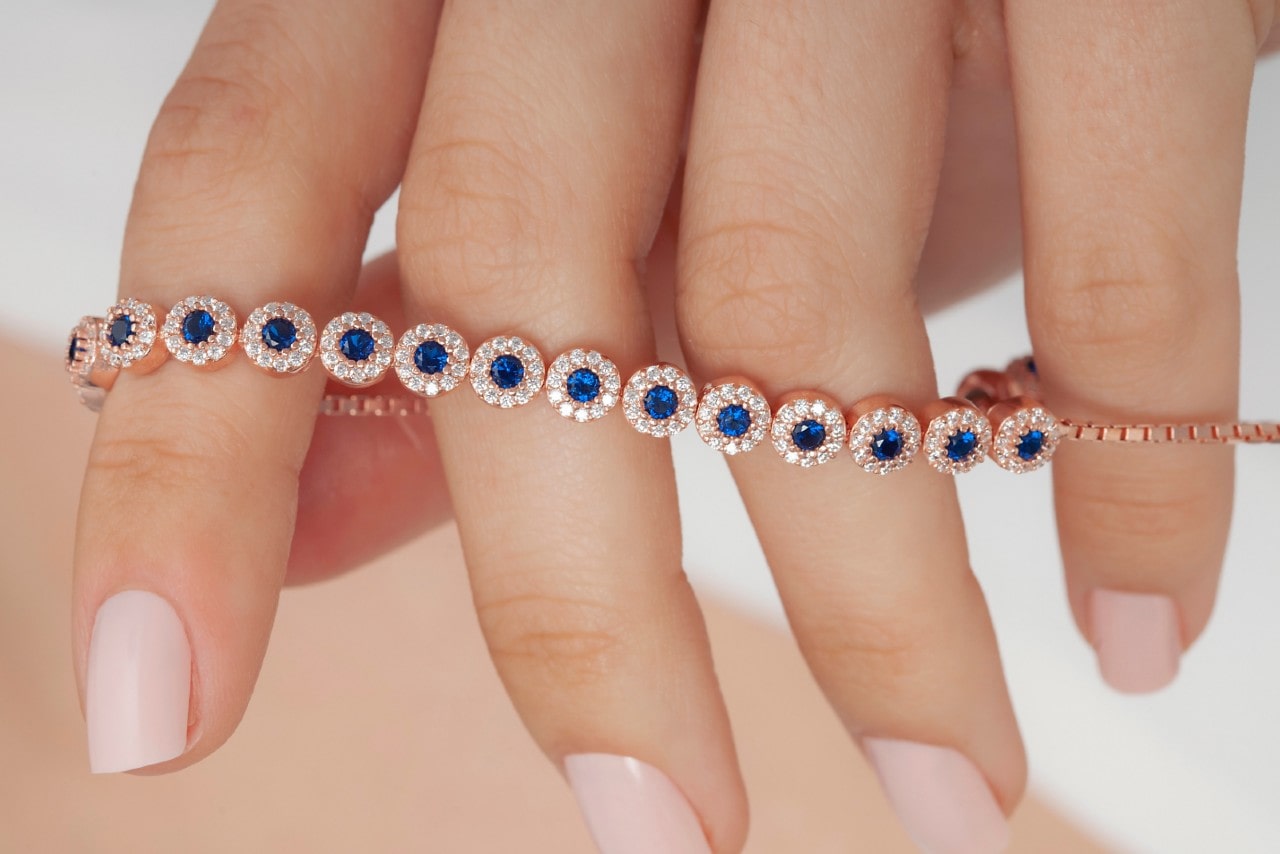 a woman’s hand holding a rose gold line bracelet featuring halo set sapphires