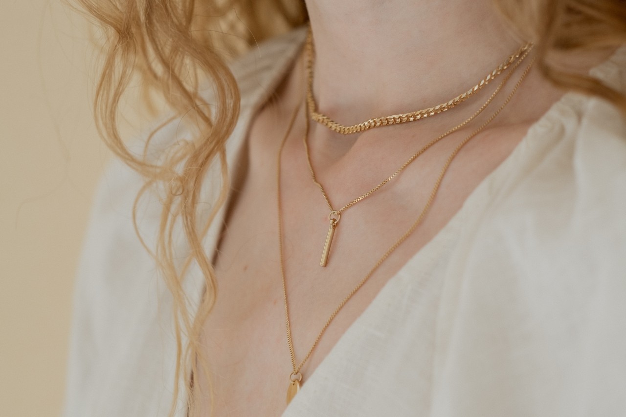 close up image of a woman’s neckline, adorned with three yellow gold necklaces