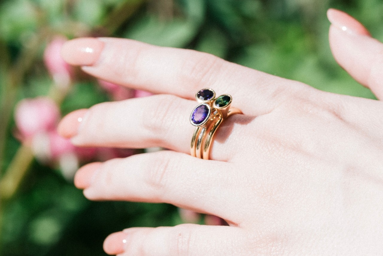 a woman’s hand wearing three stacked gemstone rings