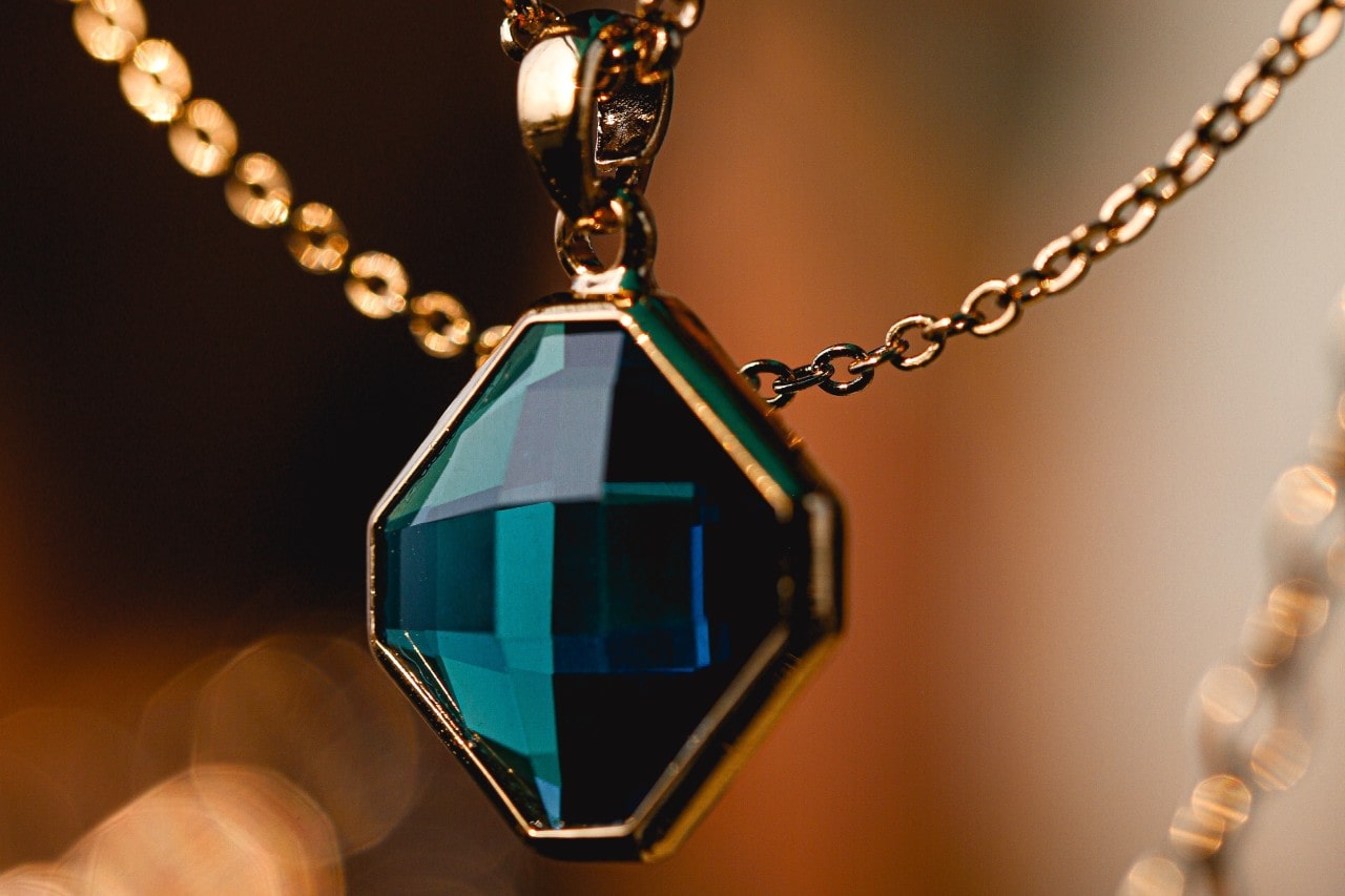 a yellow gold pendant necklace with a geometric pendant with a blue stone