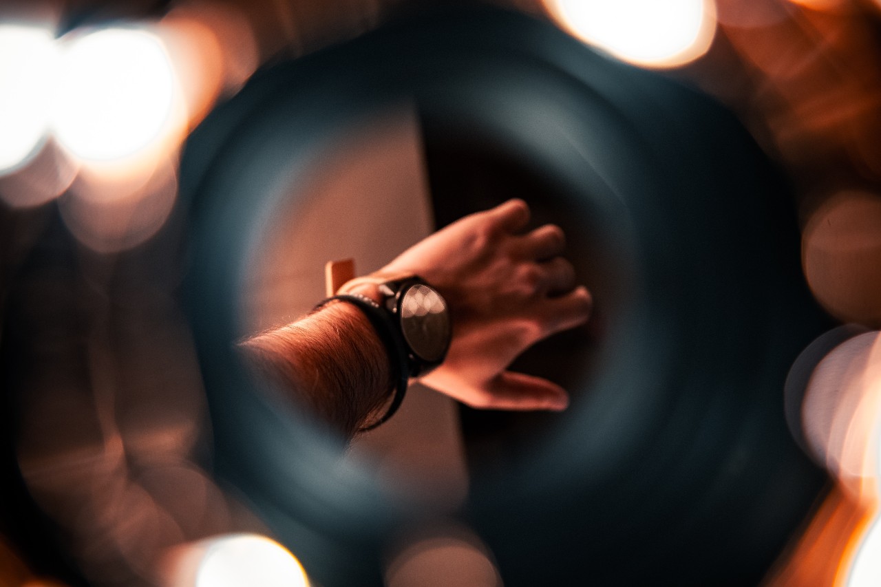 An outstretched hand wearing a large black watch, seen through a round lens