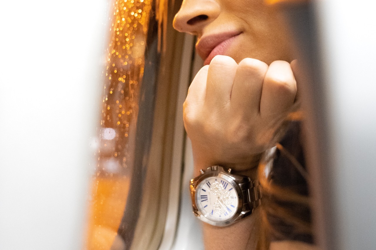 Image of a woman looking out of an airplane window, wearing a large, luxury watch
