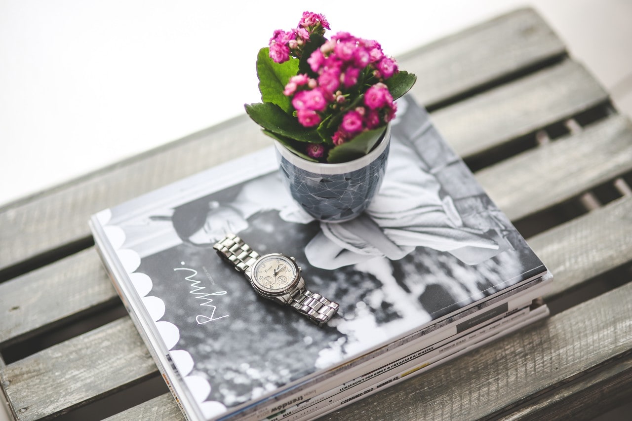 A silver watch sitting on a black and white coffee table book next to a pot of flowers