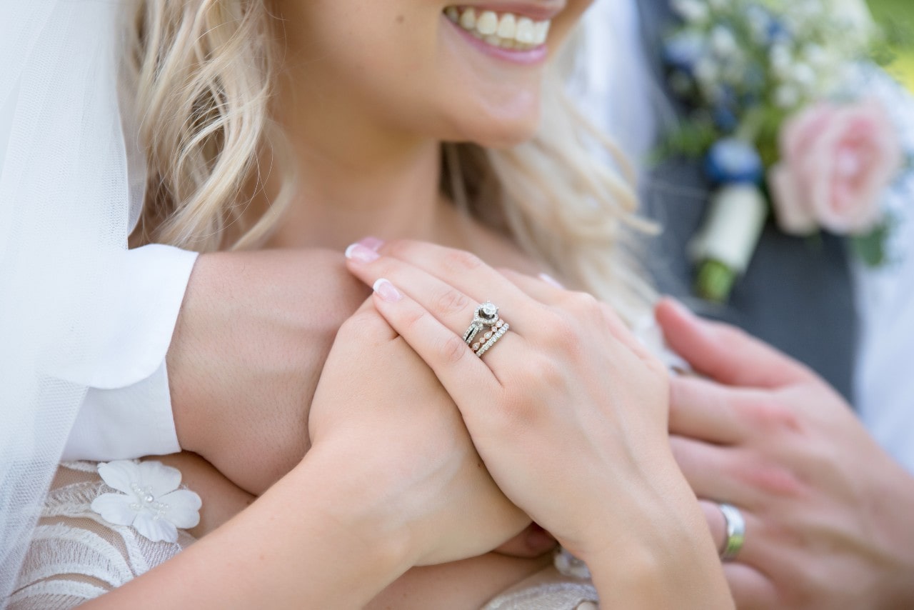Close-up of a smiling woman&rsquo;s hand wearing an engagement ring, gently resting on her husband&rsquo;s hand.