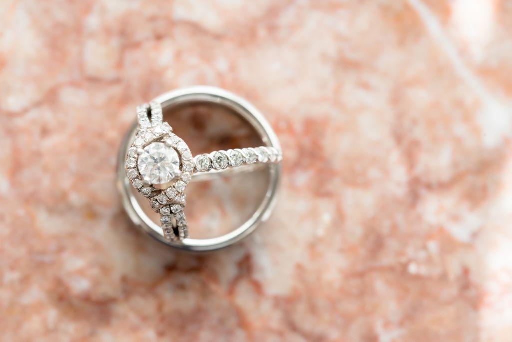 A round stone engagement ring with a beautiful halo sitting on a metal contraption over a pink marble table.