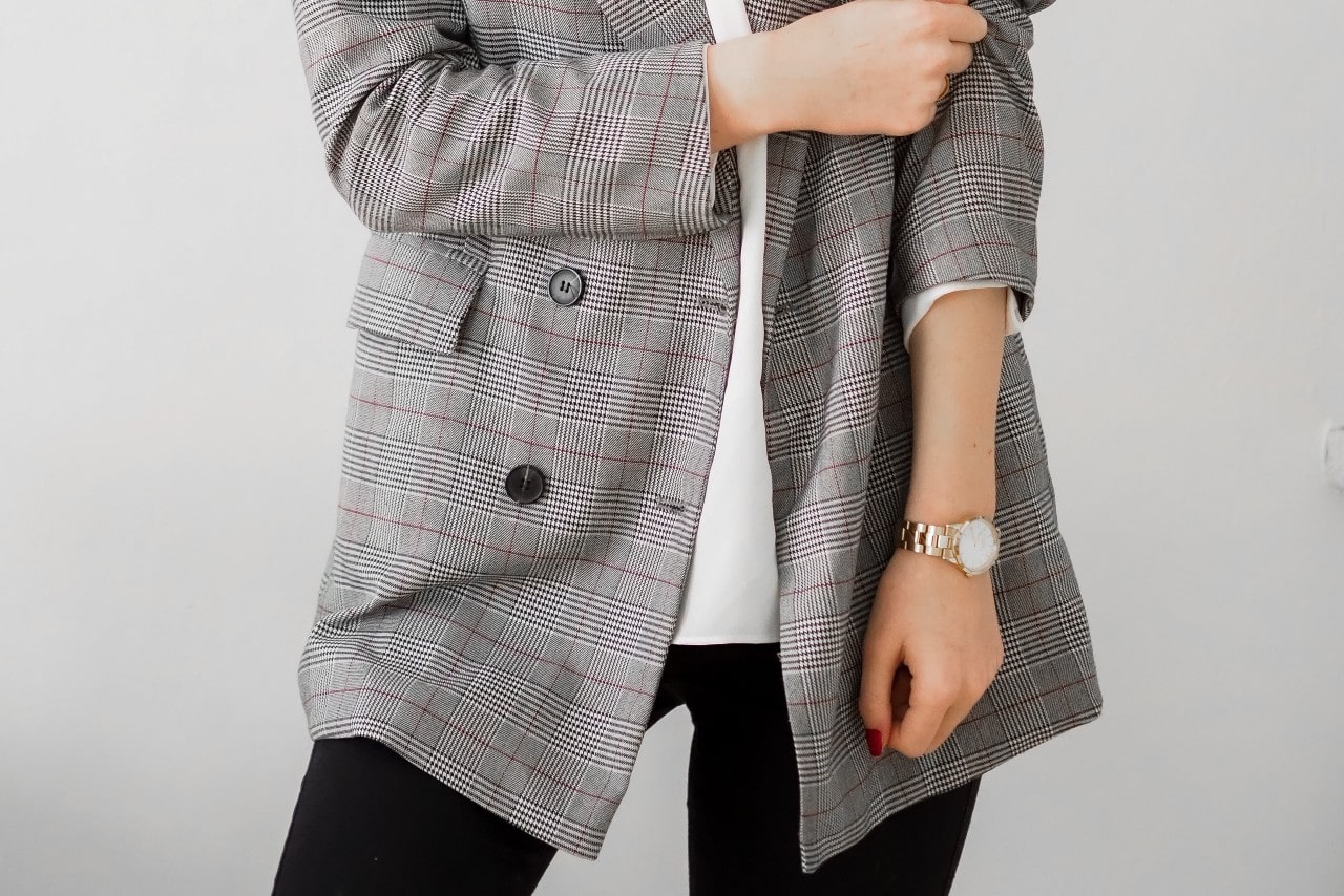 close up image of a woman in a plaid blazer and wearing a yellow gold watch