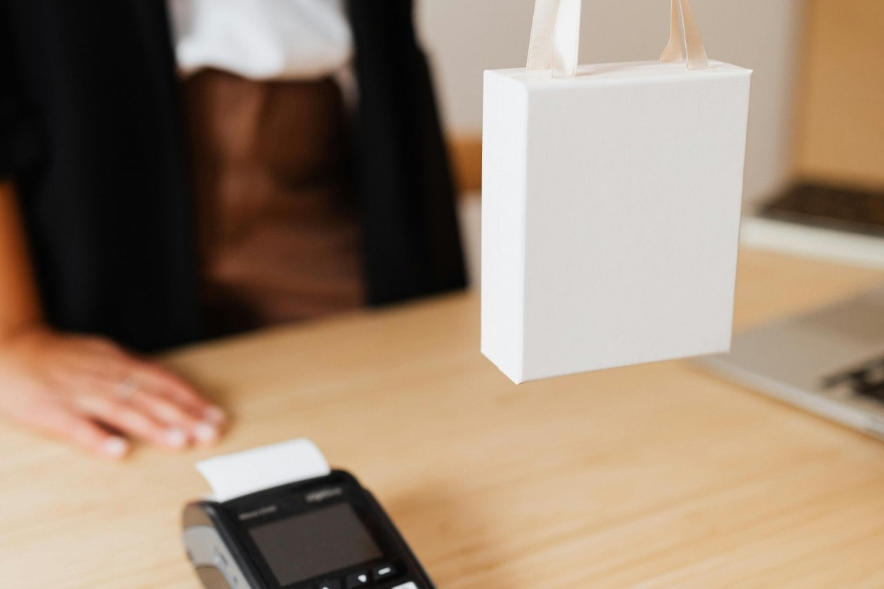 A cashier holds a white bag on top of the wooden desk with a terminal.