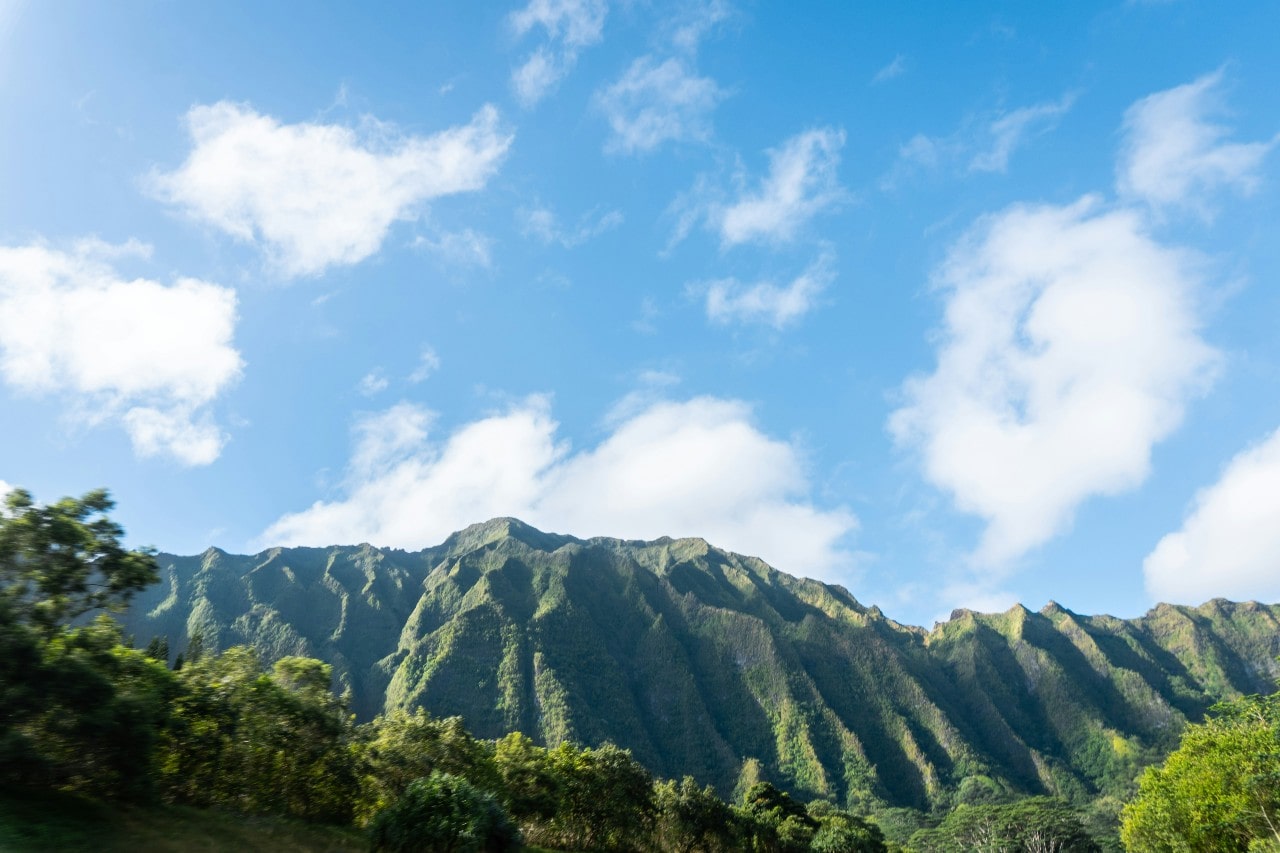 A view of tropical mountains full of green trees and a blue sky with a few clouds.