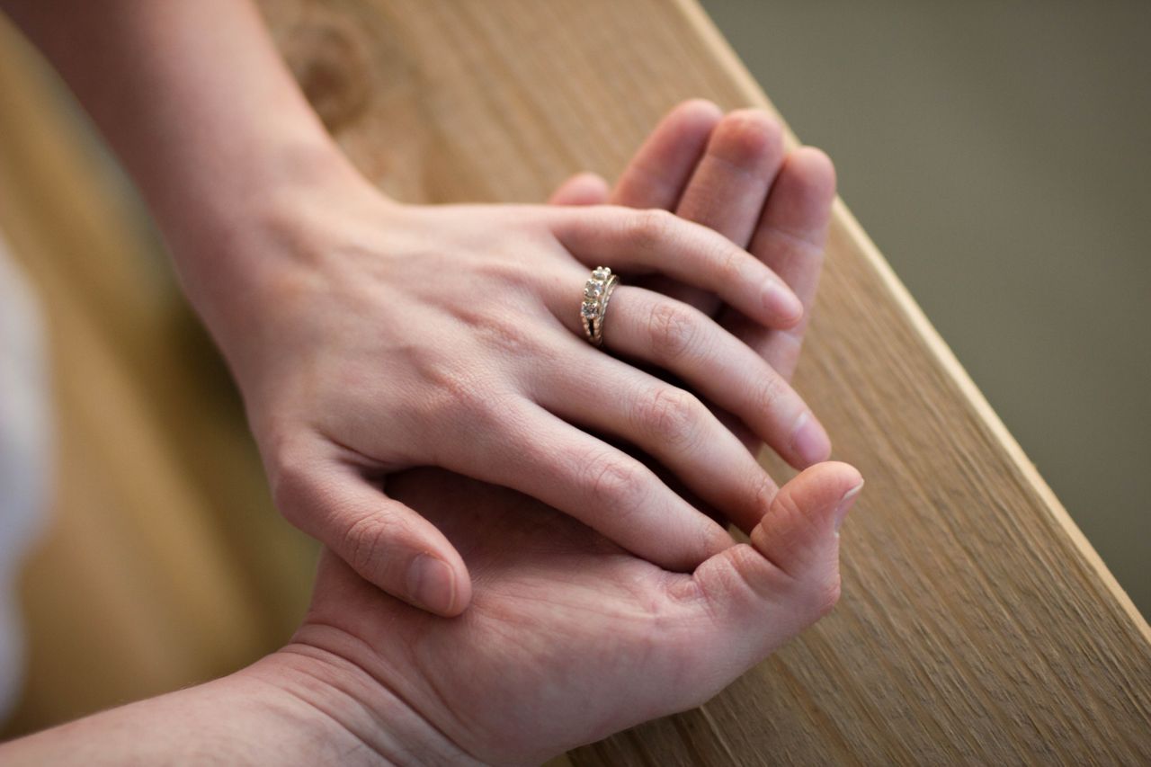 A woman resting her hand on top of her partners, showcasing her beautiful engagement ring.