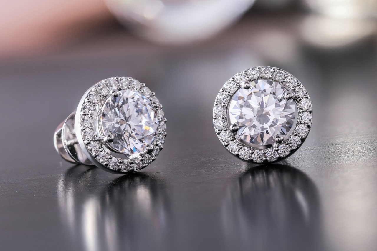 a pair of diamond halo stud earrings on a silvery surface