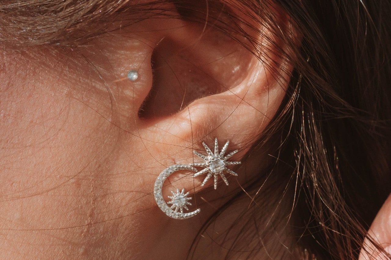 close up image of a woman’s ear wearing two diamond stud earrings, one a sun and one a moon