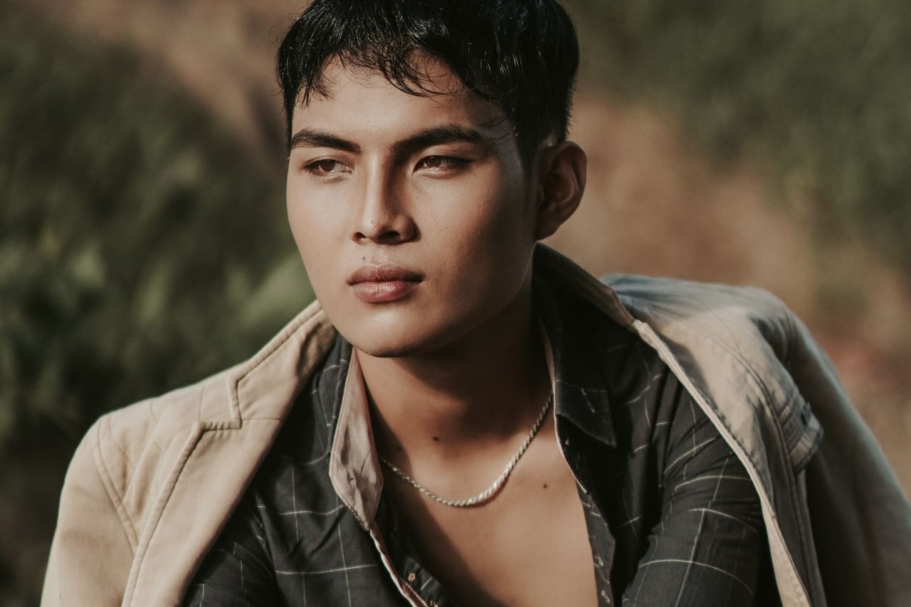 a man looking away from the camera wearing layered shirts and a silver chain necklace