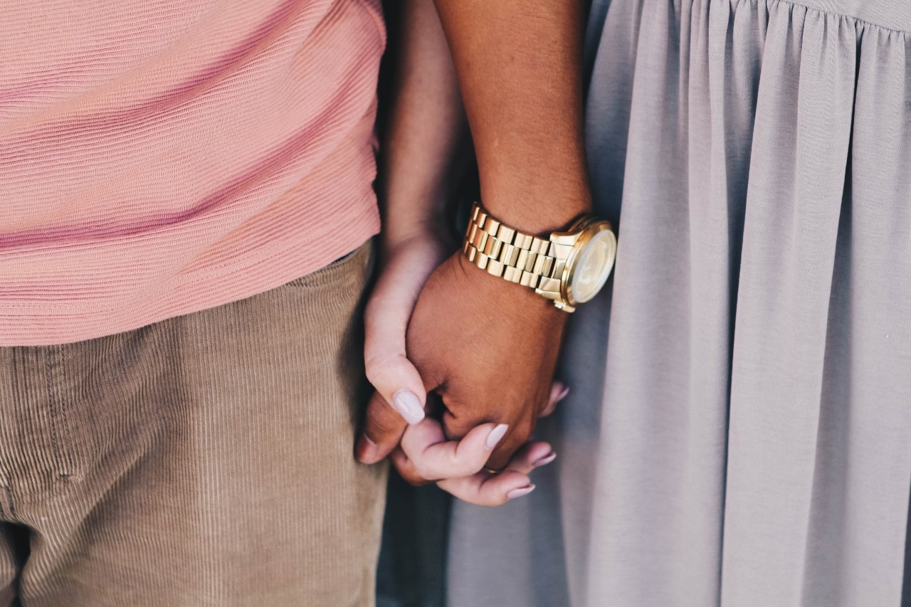 a couple holding hands, the man wearing a yellow gold watch