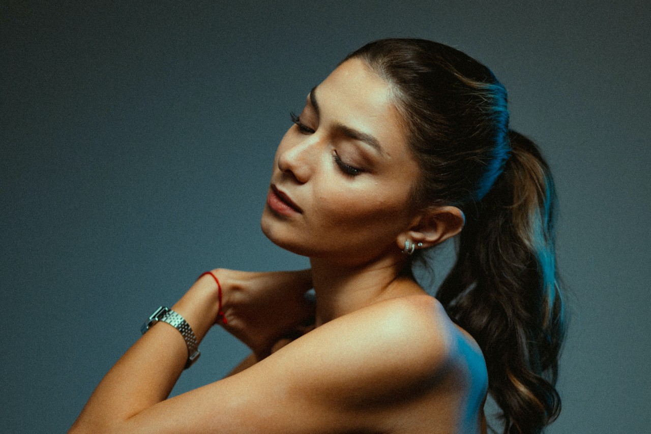 a woman with a ponytail touching her opposite shoulder and wearing a silver watch