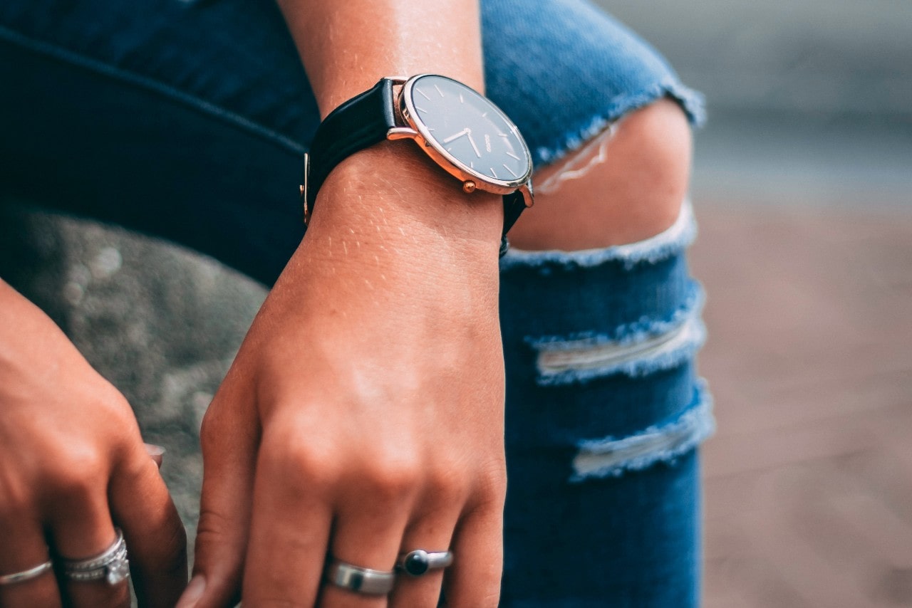 close up image of a person leaning their arms on their legs, wearing a black and gold watch and silver rings