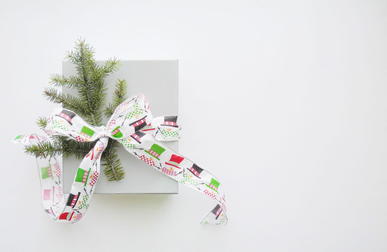 A top-down view of a simple grey gift box decorated with a whimsical snowman ribbon and a sprig of pine.