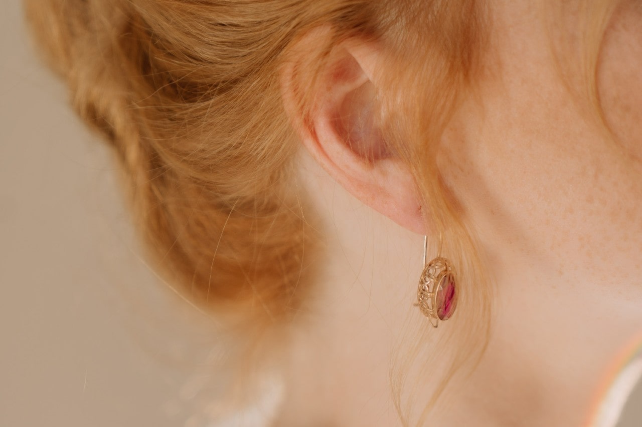 close up image of a woman with red hair in an updo wearing a pair of red gemstone earrings