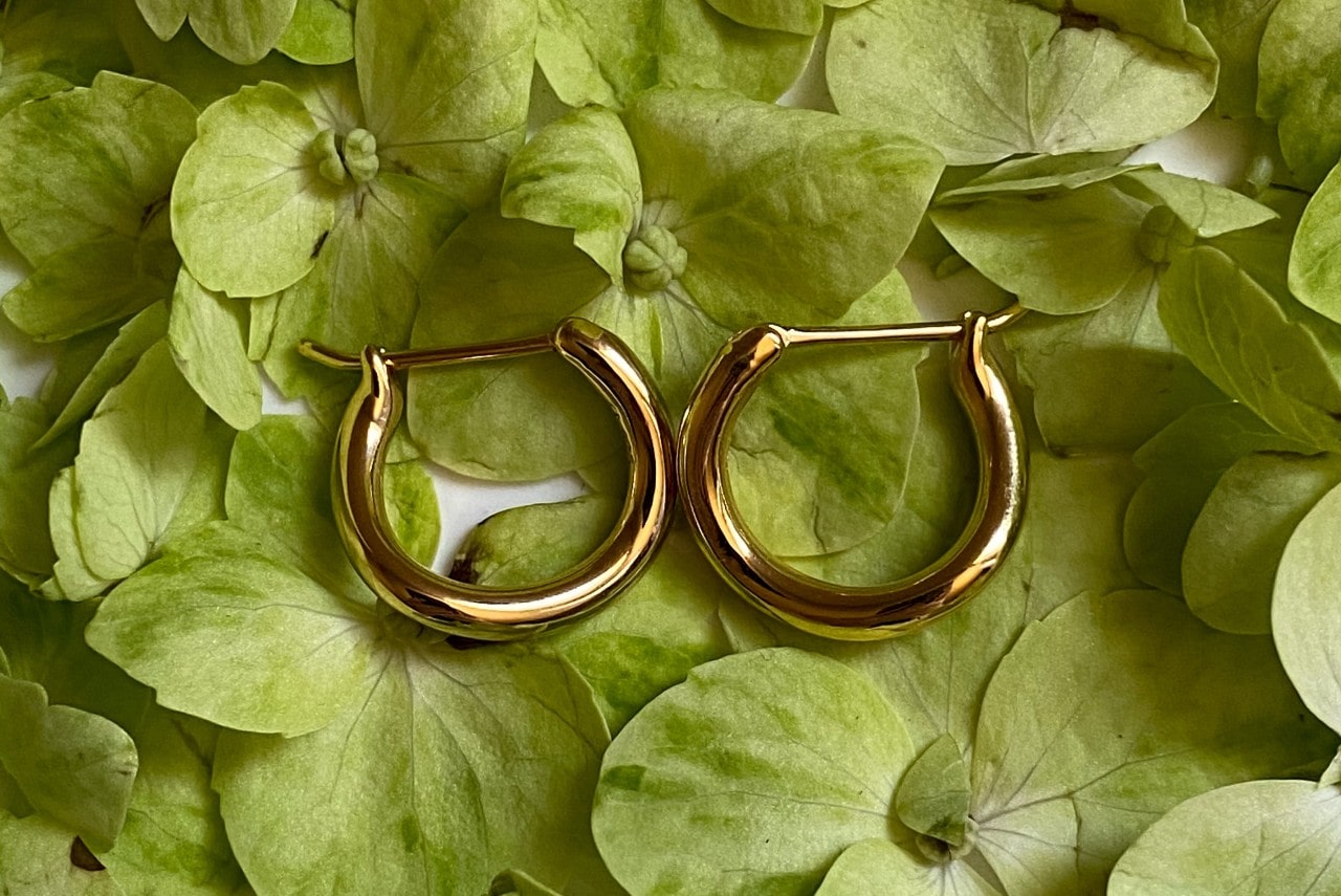 a pair of yellow gold huggies earrings lying on a bed of fresh green leaves