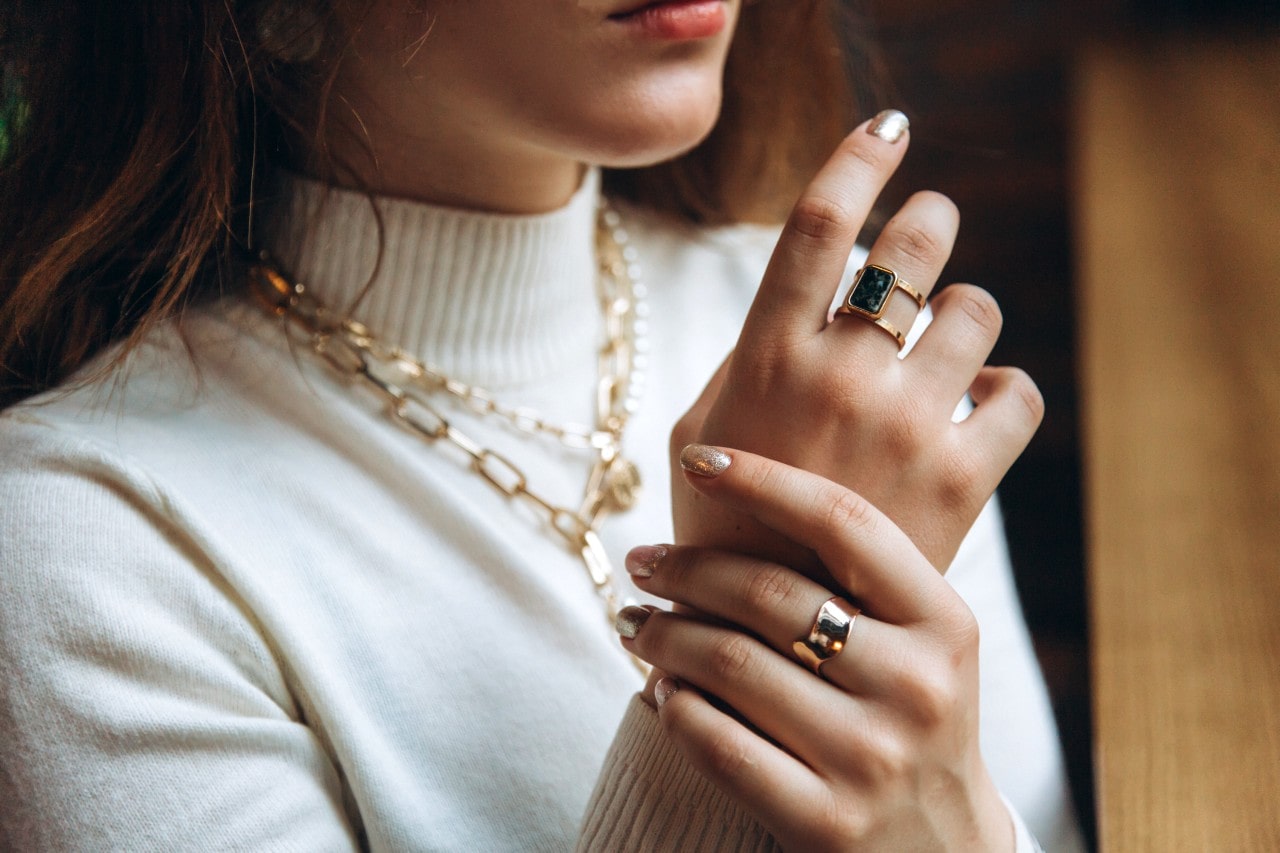 A close up of a woman in white turtleneck, showcasing yellow chunky jewelry, from chain layered necklaces to fashion rings.
