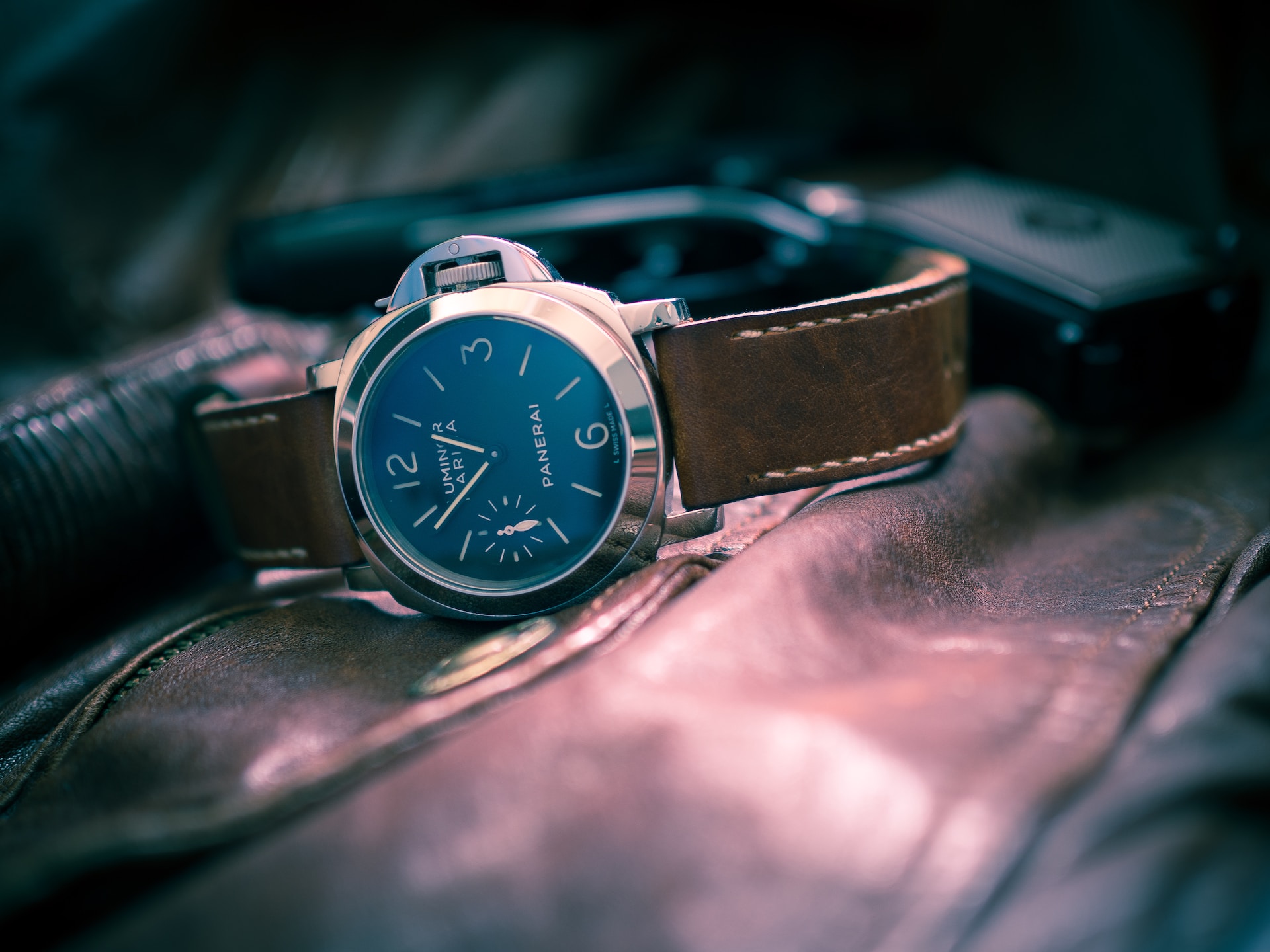 A luxury wristwatch with a brown leather strap and a black dial rests on a leather surface.