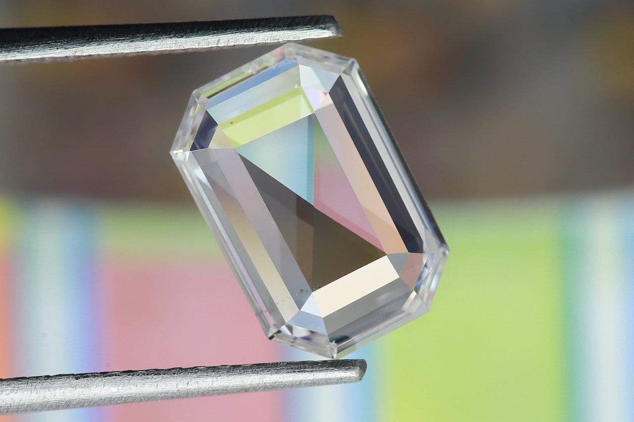 A close-up of an emerald-cut diamond held by tweezers against a blurry background