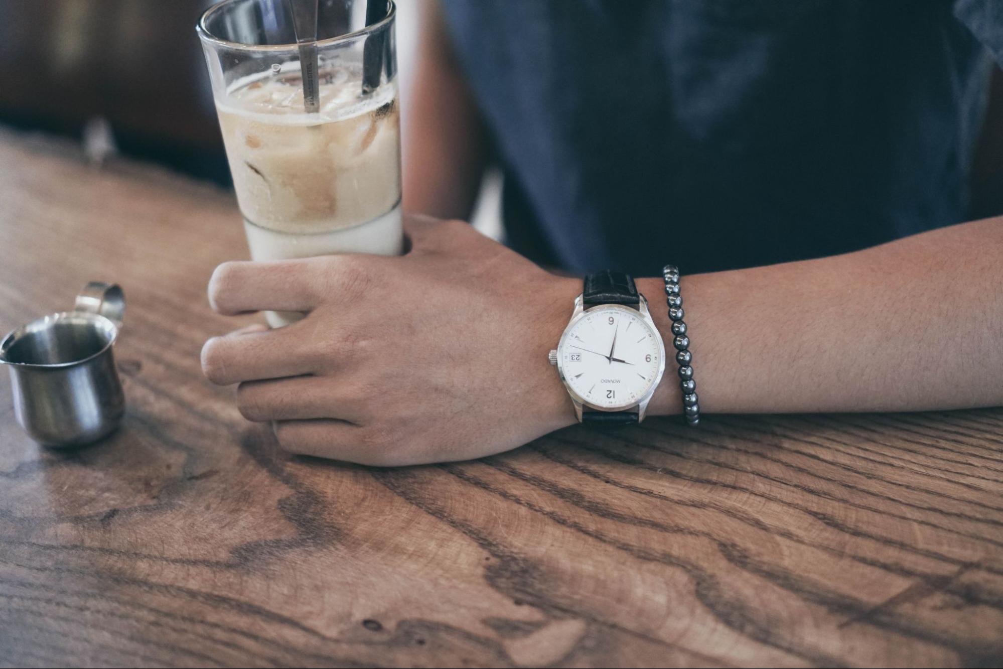 a hand holding a glass and wearing a watch and bracelet