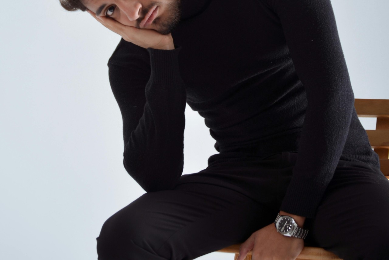 a man in all black sitting in a chair and wearing a silver and black watch