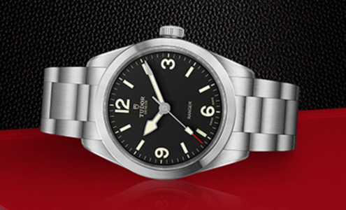A close-up of a TUDOR Ranger watch displayed on its side on a red and black background.
