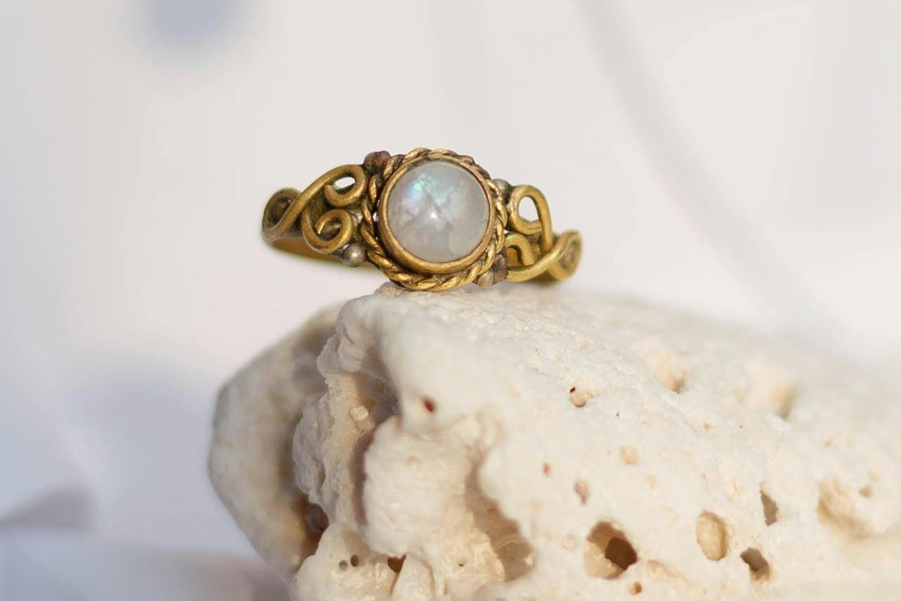 A moonstone gemstone set in an entwined gold setting sitting on a piece of dried coral.