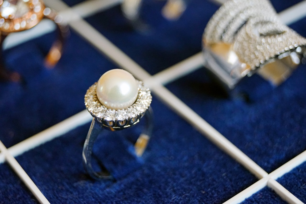 A blue velvet ring holder with a silver pearl and diamond fashion ring, alongside other rings.