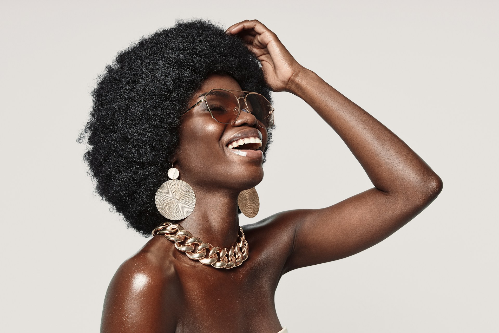 A woman with an afro hairstyle and sunglasses wearing a pair of statement earrings and a bold chain necklace.