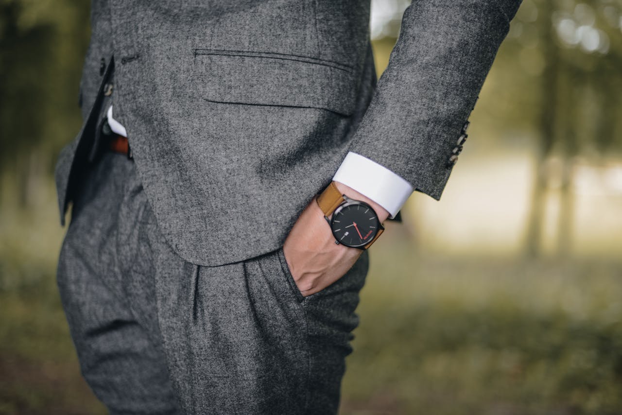 A close-up of a well-dressed man in a suit wearing a luxury watch outdoors.