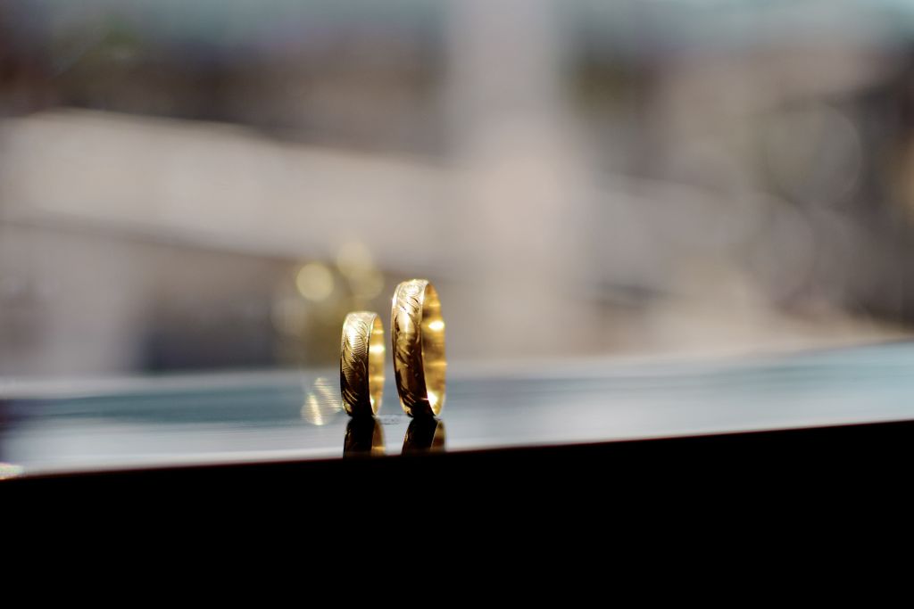 Two yellow gold wedding bands standing on their sides on the ledge of a window, the background blurred.