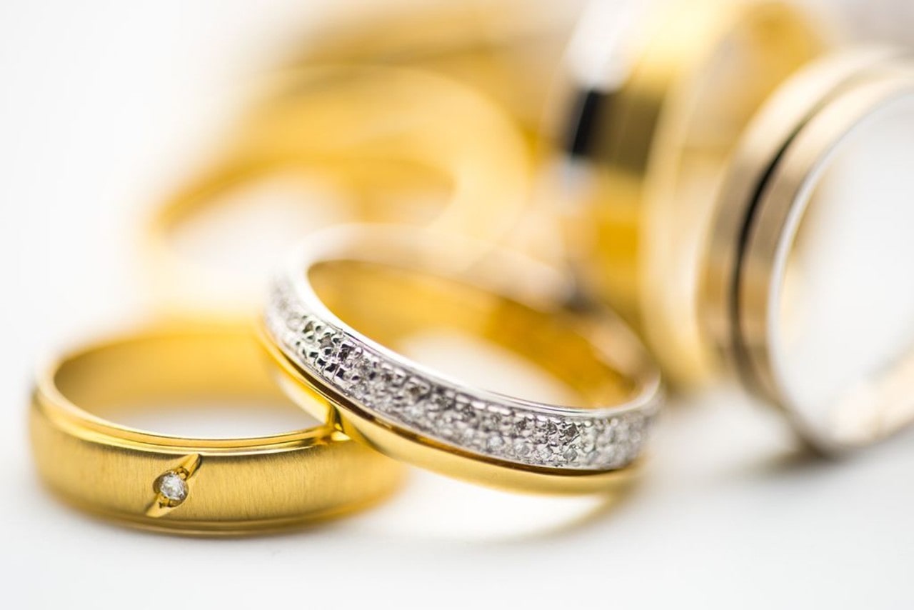 A bunch of yellow gold wedding bands with different diamond accents all laying on a white surface.