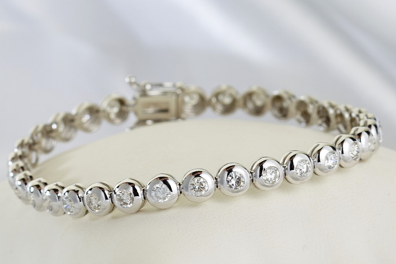 A close-up of a white gold diamond bezel set tennis bracelet on a white surface.
