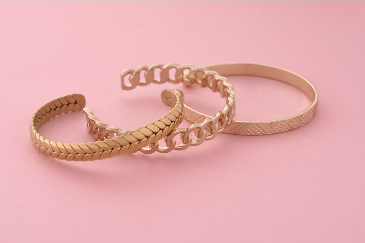 Three yellow gold open bangles on a pink surface