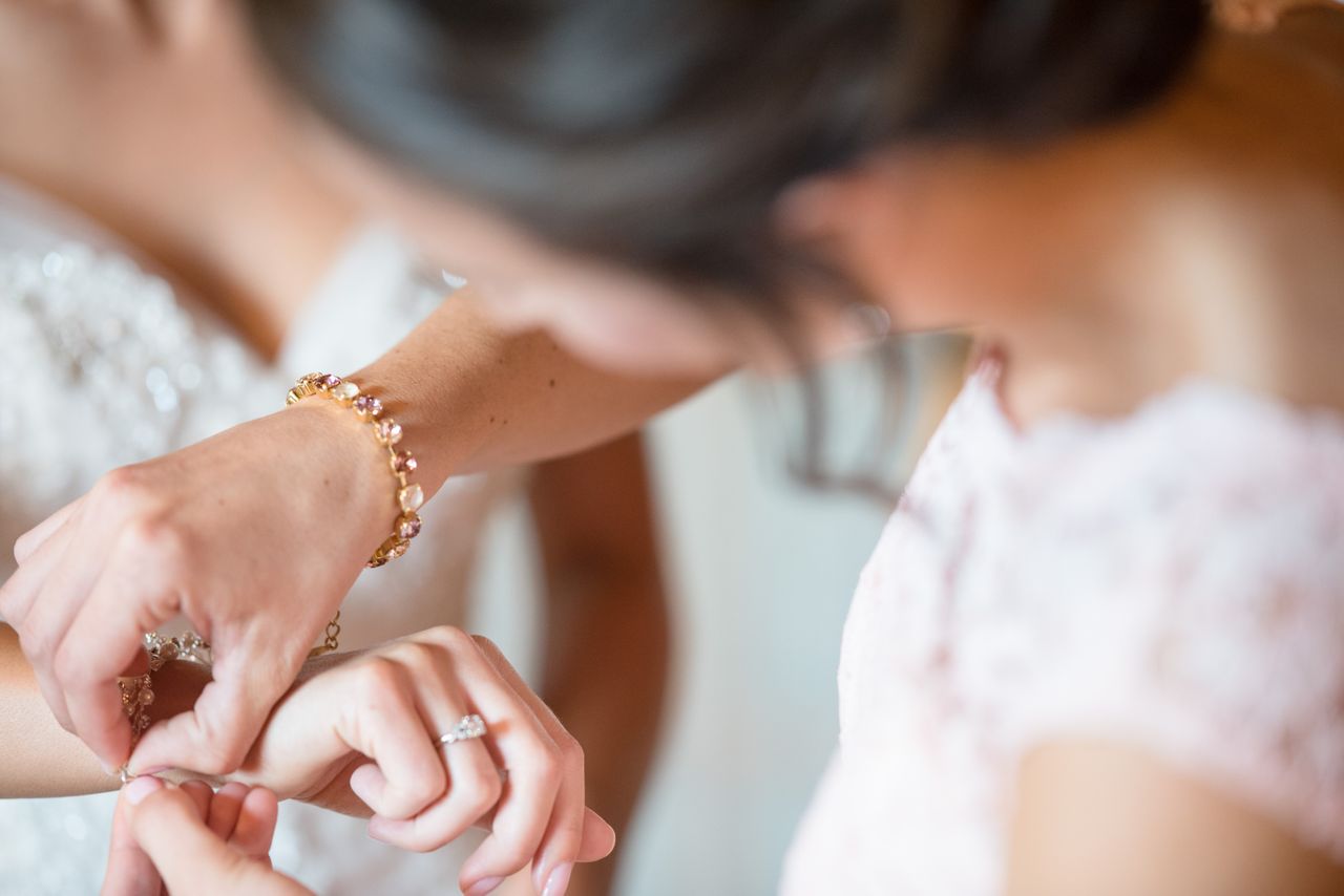 A close-up of a woman with a gemstone yellow gold bracelet fixing a bracelet on a bride’s hand