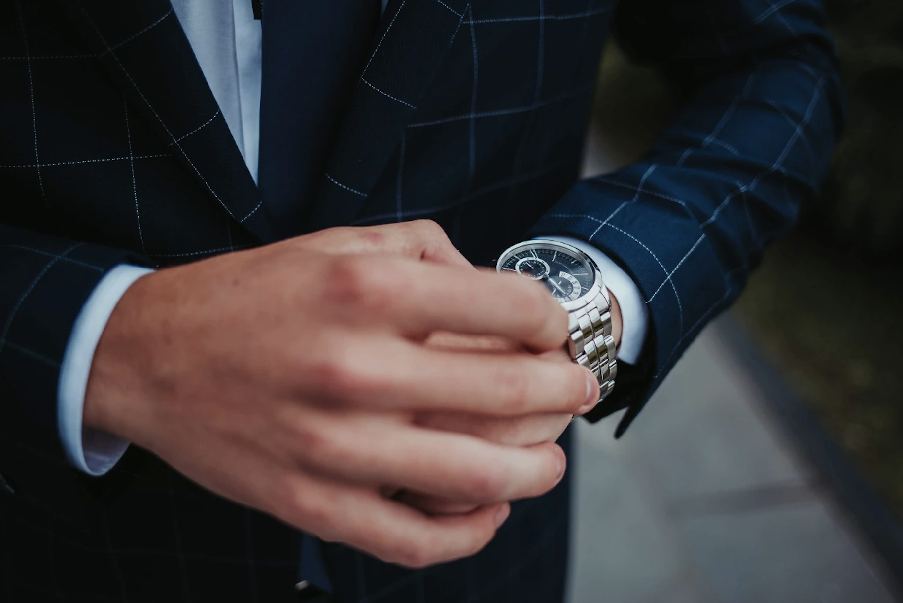 A close up of a man in checkered suit checking with metallic wristwatch