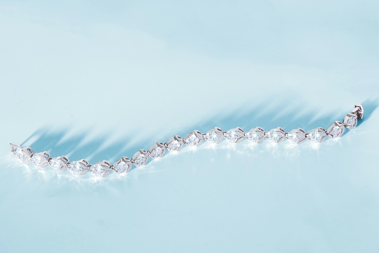 A close-up of a glistening tennis bracelet decoratively displayed on a sky blue background.