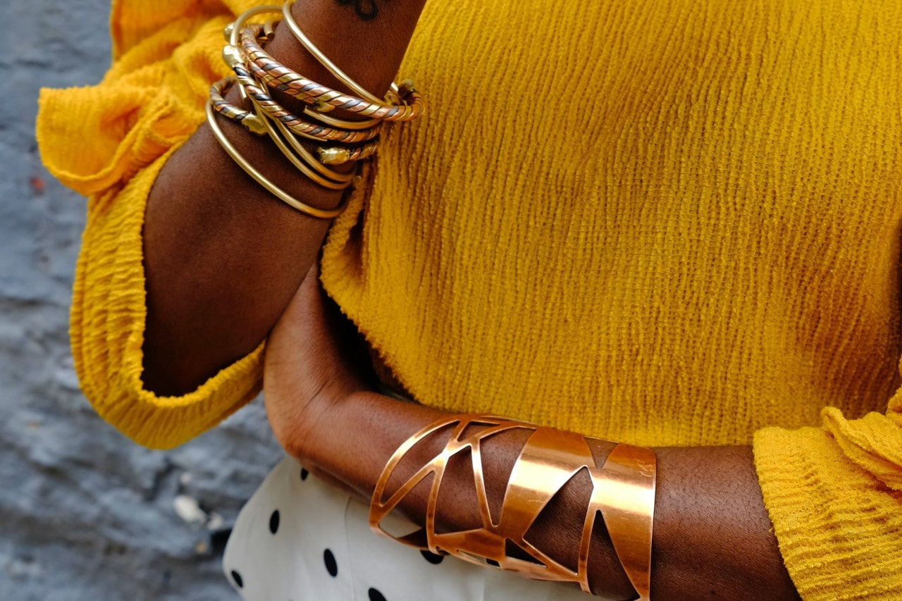 A close-up of a woman’s wrists, her left wrist clad in a bold cuff, and her right adorned in multiple stacked bangles.