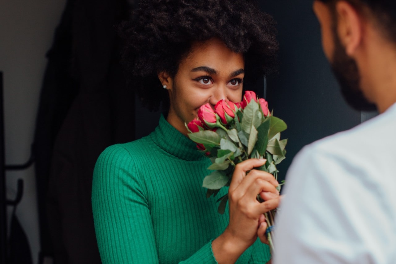 a woman sniffs the bouquet of roses her beloved has given her.