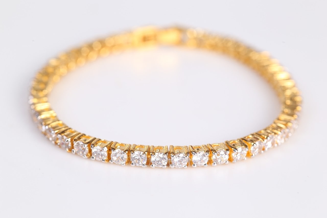 A close-up of a gold tennis bracelet with round cut diamonds on white background.