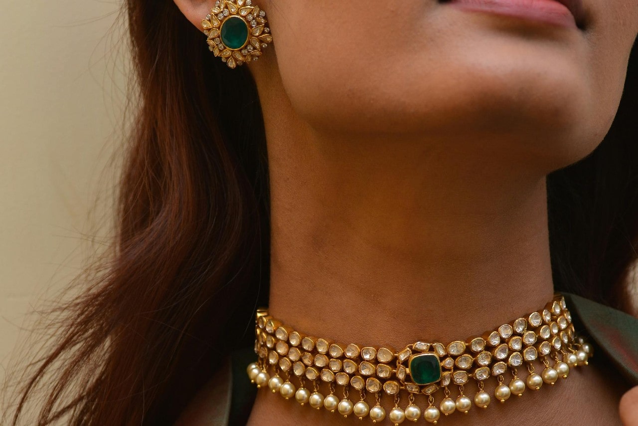 A close-up of a woman’s neck adorned in an ornate gold choker with pearls and precious stones, paired with matching earrings.