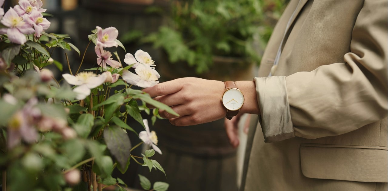 a woman outside reaching for a flower, wearing a yellow gold and leather watch