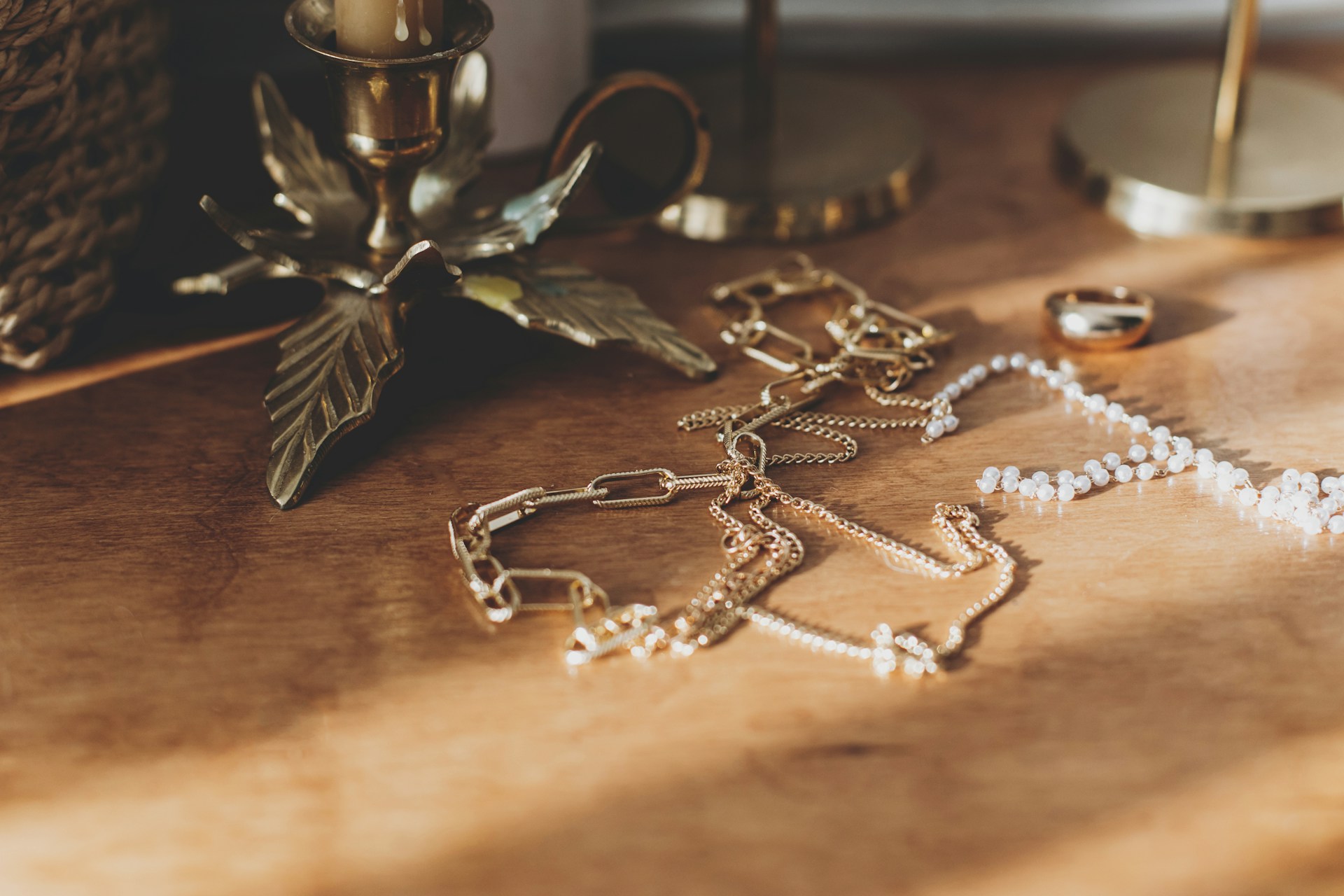 A collection of yellow gold chain necklaces displayed atop a wooden counter next to vintage candelabras.