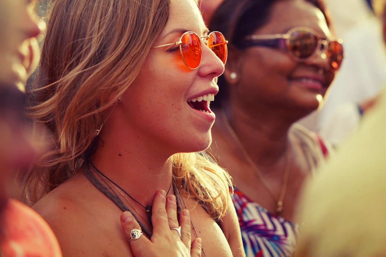 A view of two happy women on a bright day, both wearing colorful sunglasses and light jewelry.