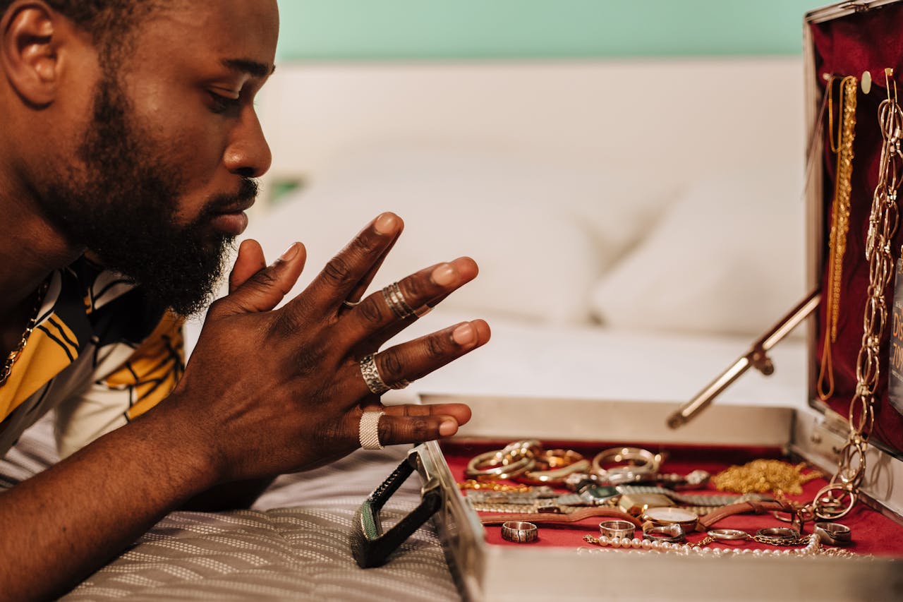 A man wearing three fashion rings on his right hand examining a slightly cluttered jewelry collection stored in an open case.
