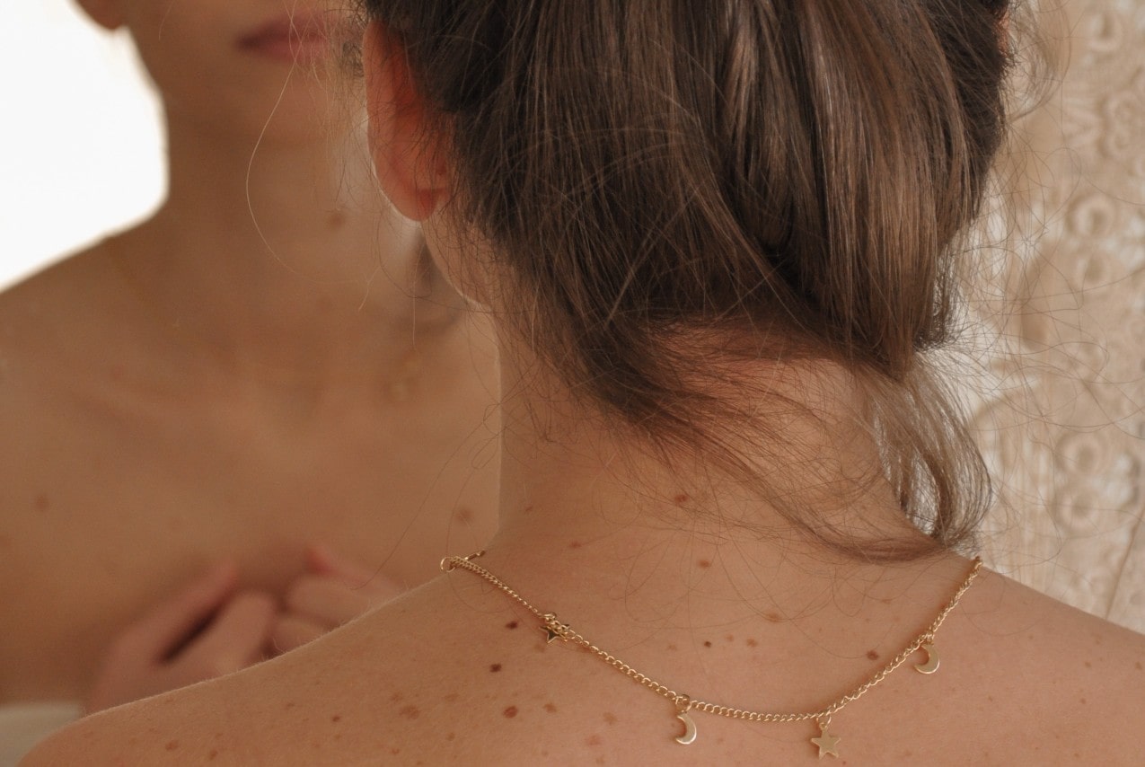 A woman, freshly out of the shower, puts on a gold station necklace.