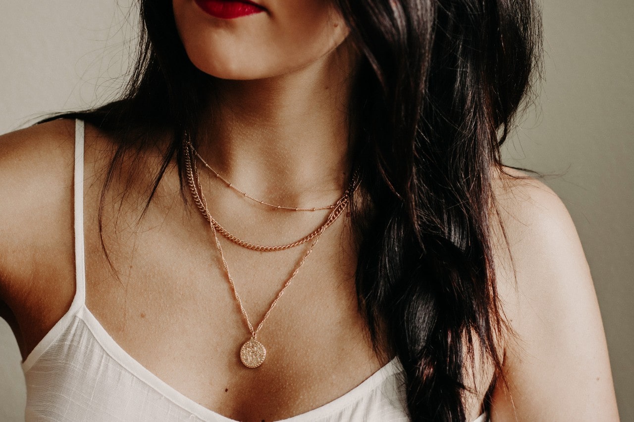 A woman in a white tank wearing a trio of gold necklaces.