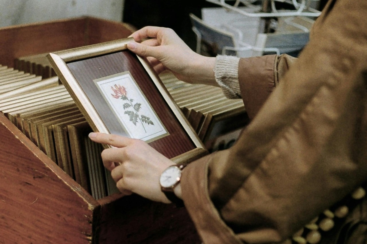 a person looking through a stack of framed photos and wearing a gold watch